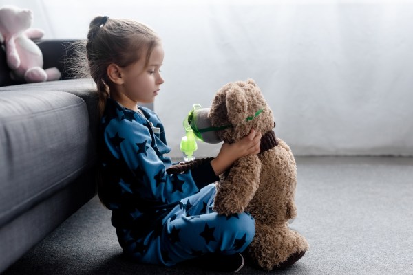 Girl looking at teddy bear wearing oxygen mask